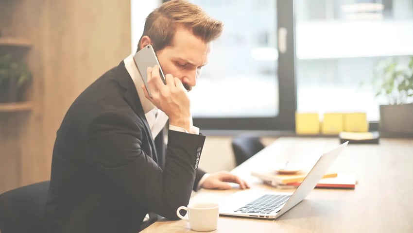 Man having a phone call in front of a laptop trying these time-tested tips & real-world scripts for P&C agents expanding into life insurance